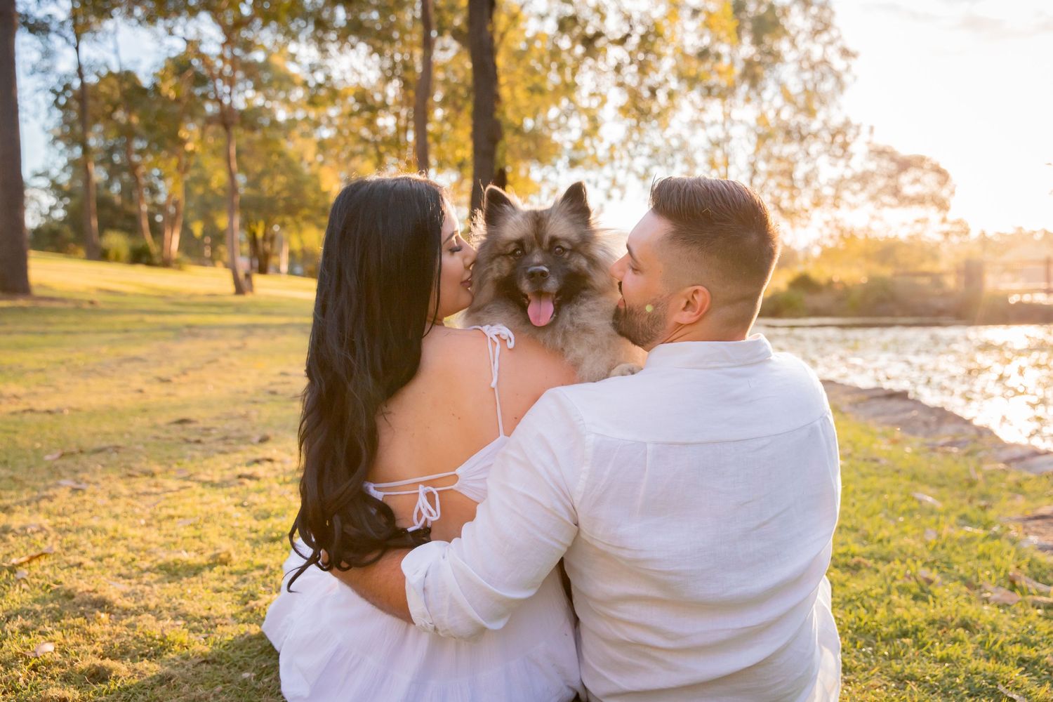 Two people look inwards as Keeshond pops its head over their shoulders and looks directly into the camera