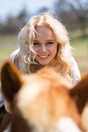 A smiling blonde woman on horseback enjoys a sunny day in an open field.