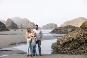 Family of three posing on a misty beach surrounded by dramatic rock formations along the Oregon coast.