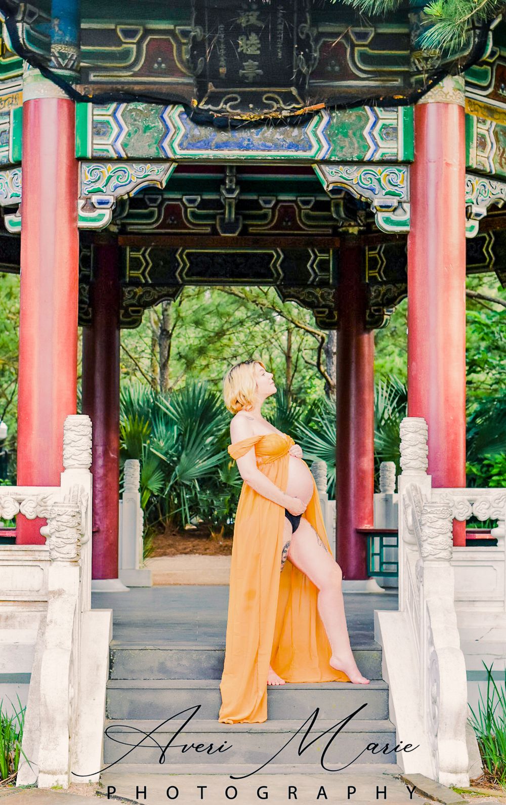 Maternity photo of a person in orange dress posing under an ornate Asian pavilion.