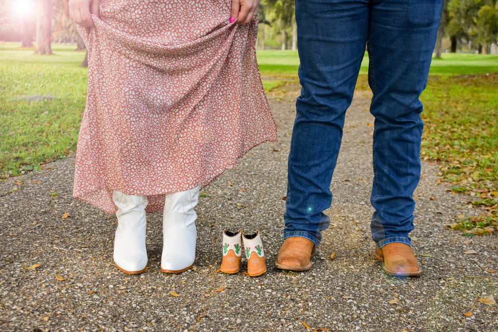 Two pairs of boots standing together on gravel path under oak trees.