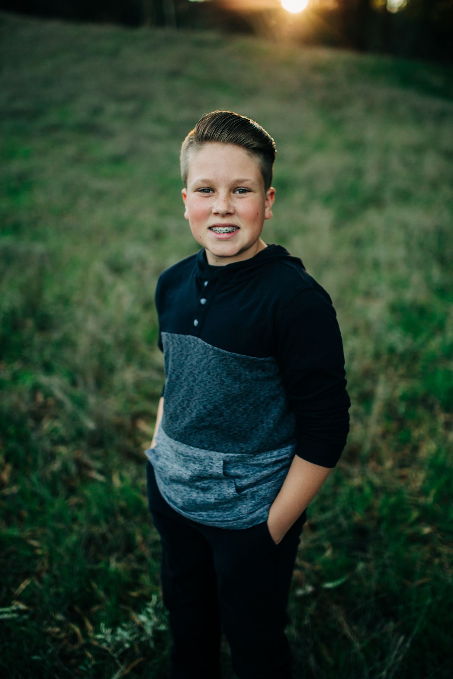 Young boy with hands in this pockets on a grassy hill with the sunset behind him, Orcutt, CA
