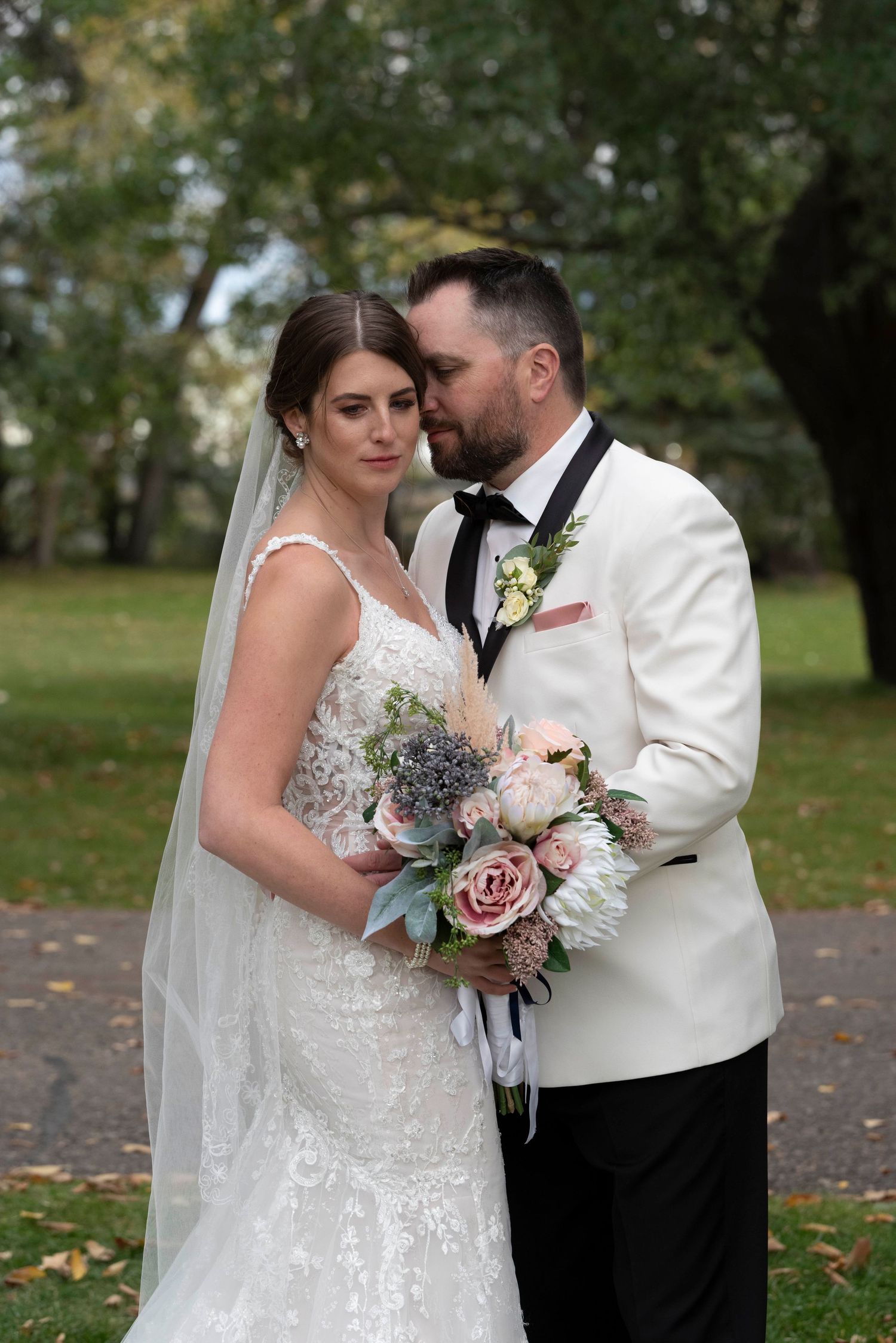 Intimate wedding portrait with couple in white attire holding delicate pink and gray bouquet.