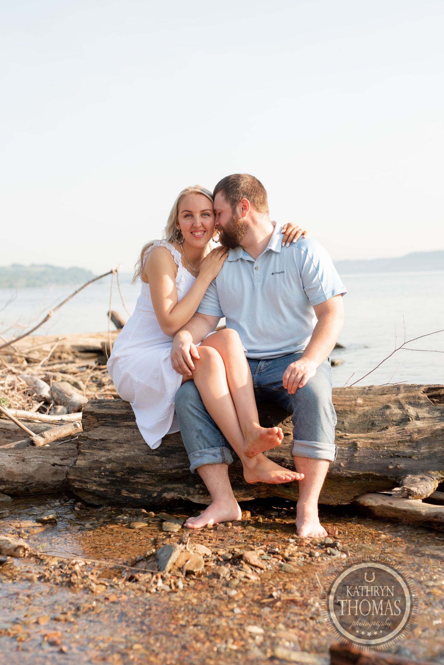 A sweet couple's portrait while sitting on driftwood by the water at sunset.