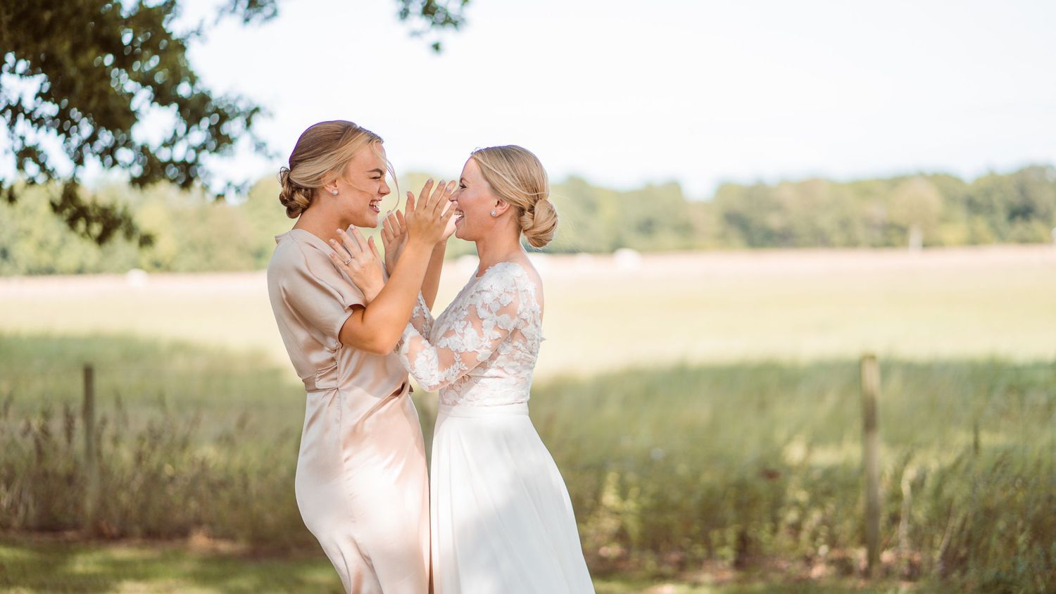 Bride and bridesmaid in champagne dress sharing a joyful moment together in sunny field.