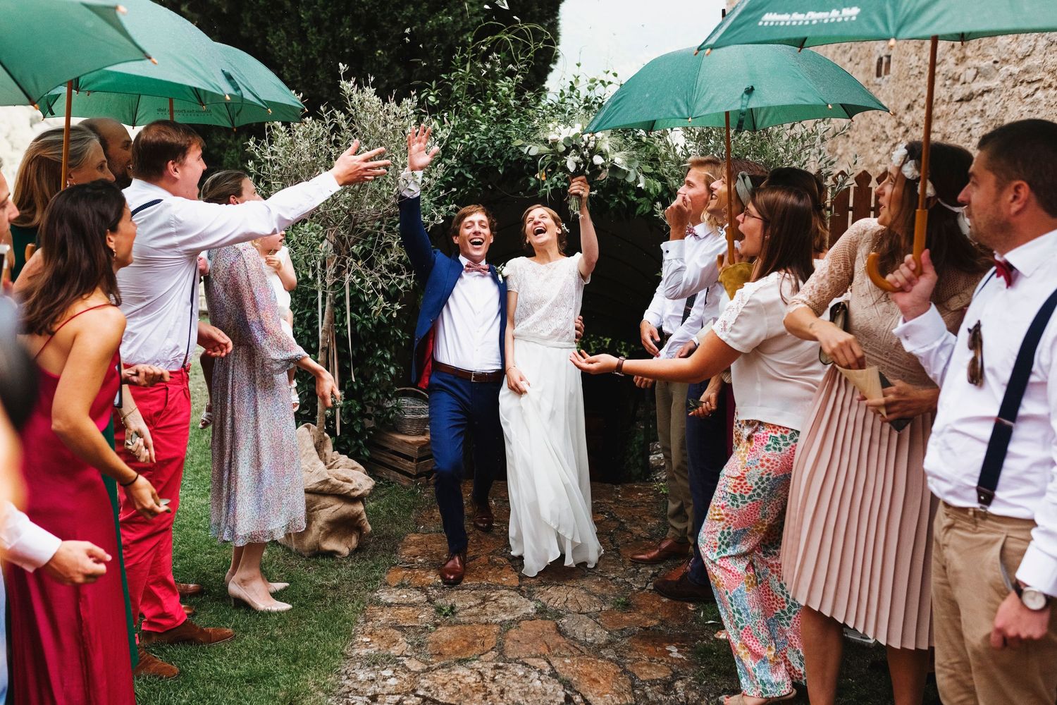 Wedding guests celebrate under green umbrellas in an outdoor garden reception setting.