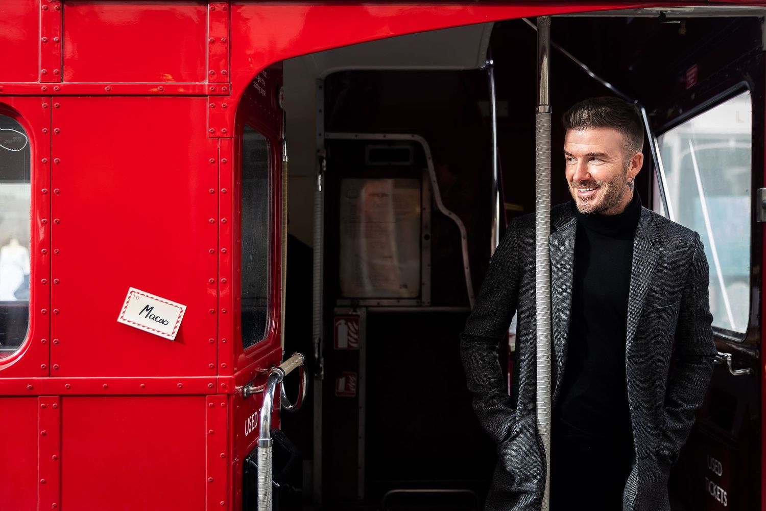 Person in dark outfit standing in doorway of bright red London bus.