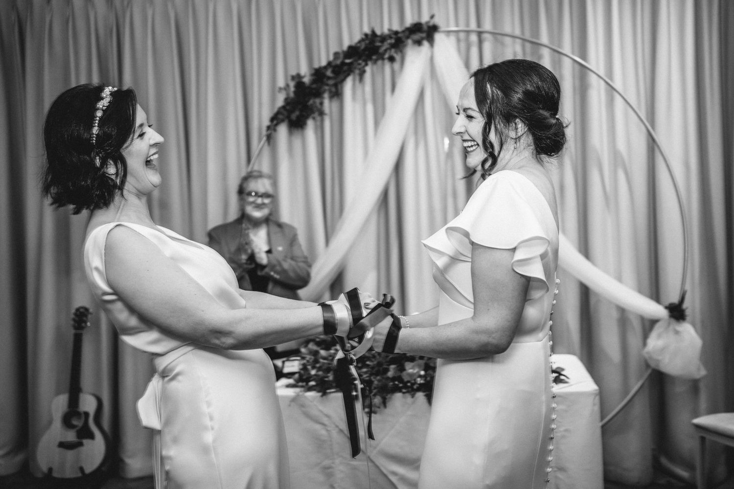 Black and white photo of a wedding ceremony under an arch with decorative greenery.