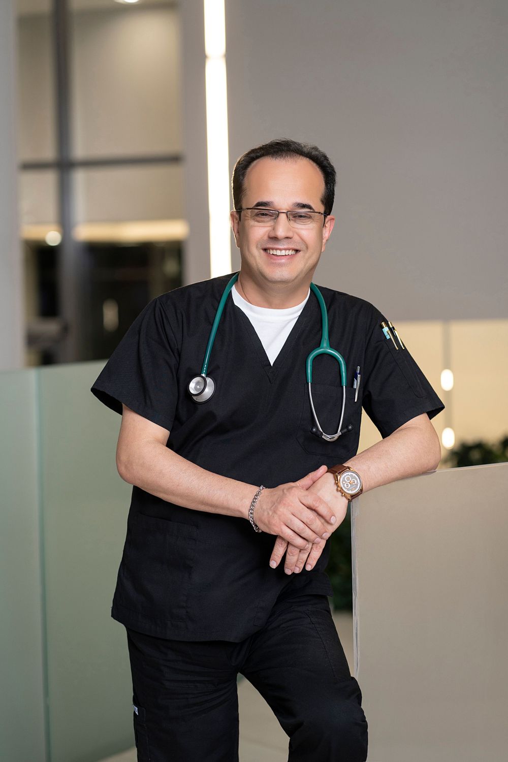 Healthcare professional in dark scrubs with stethoscope standing in a modern medical facility.