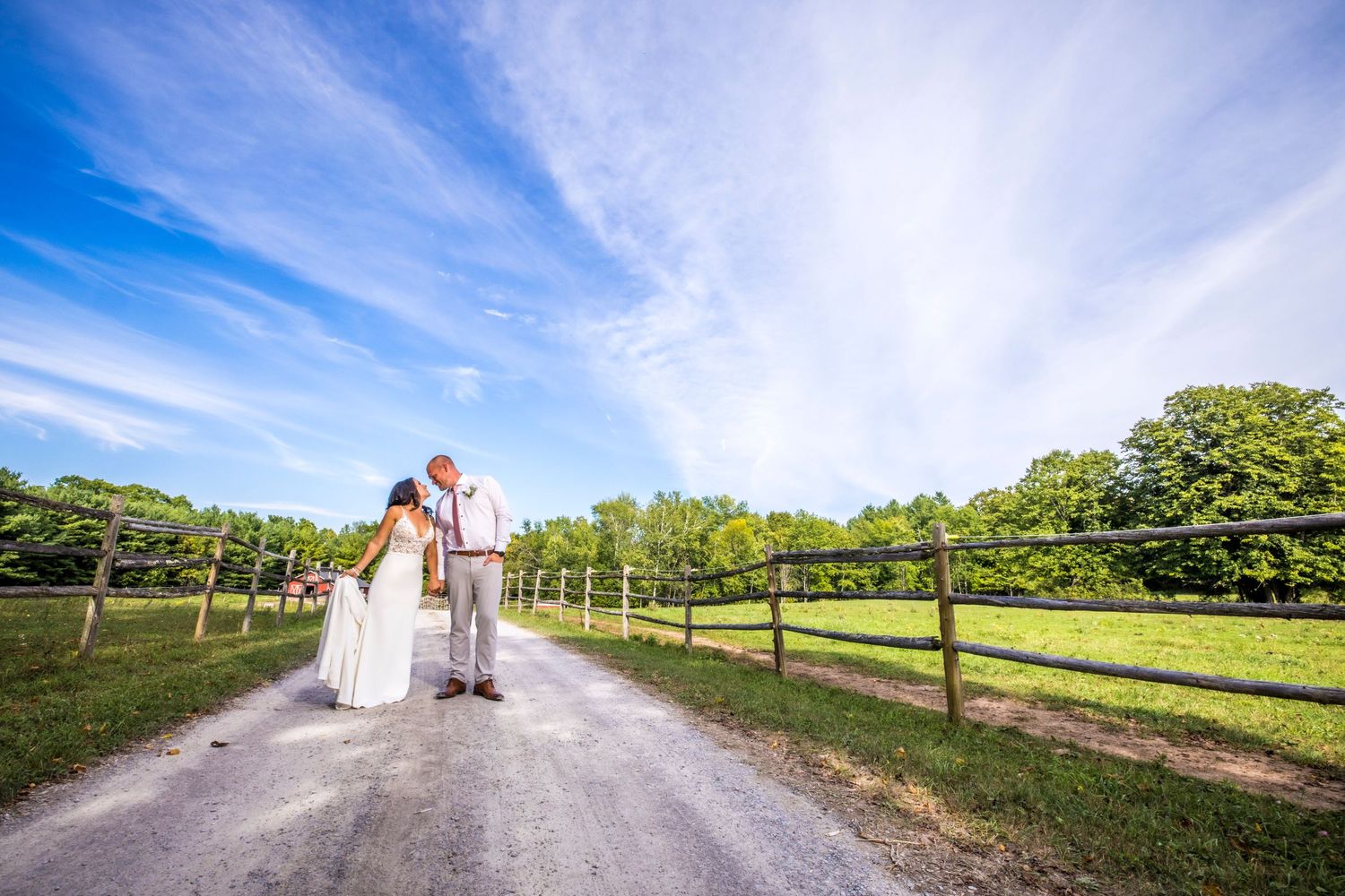 Wedding party walks along a scenic country path with blue sky and green fields on a sunny day.