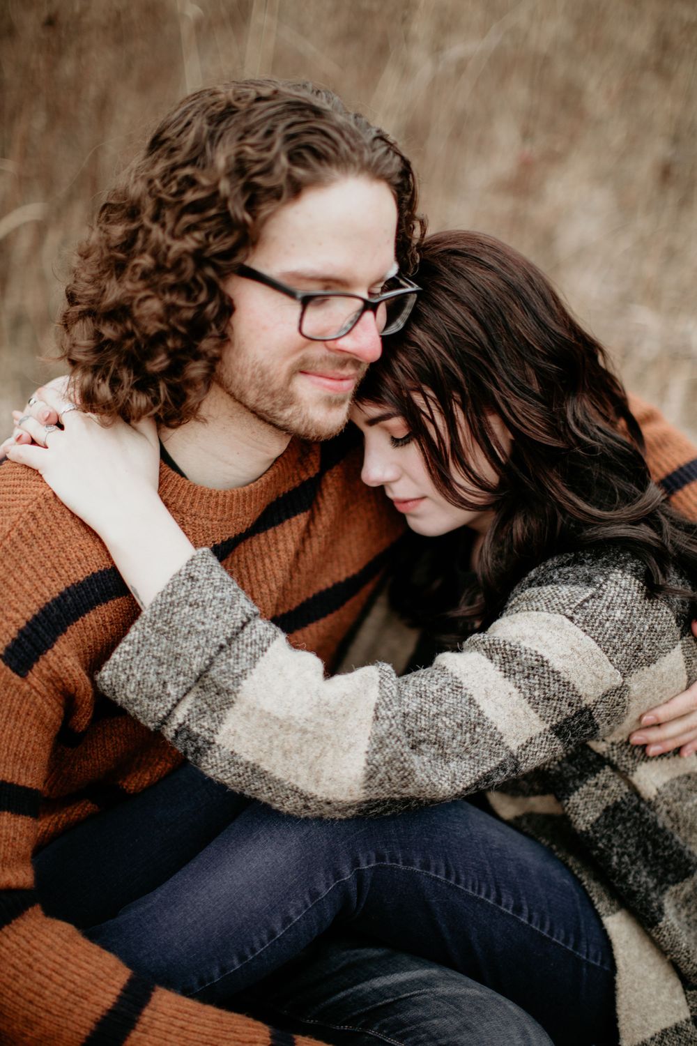 Close-up of couple cuddling, man in rust striped sweater with curly hair and glasses nuzzling woman.