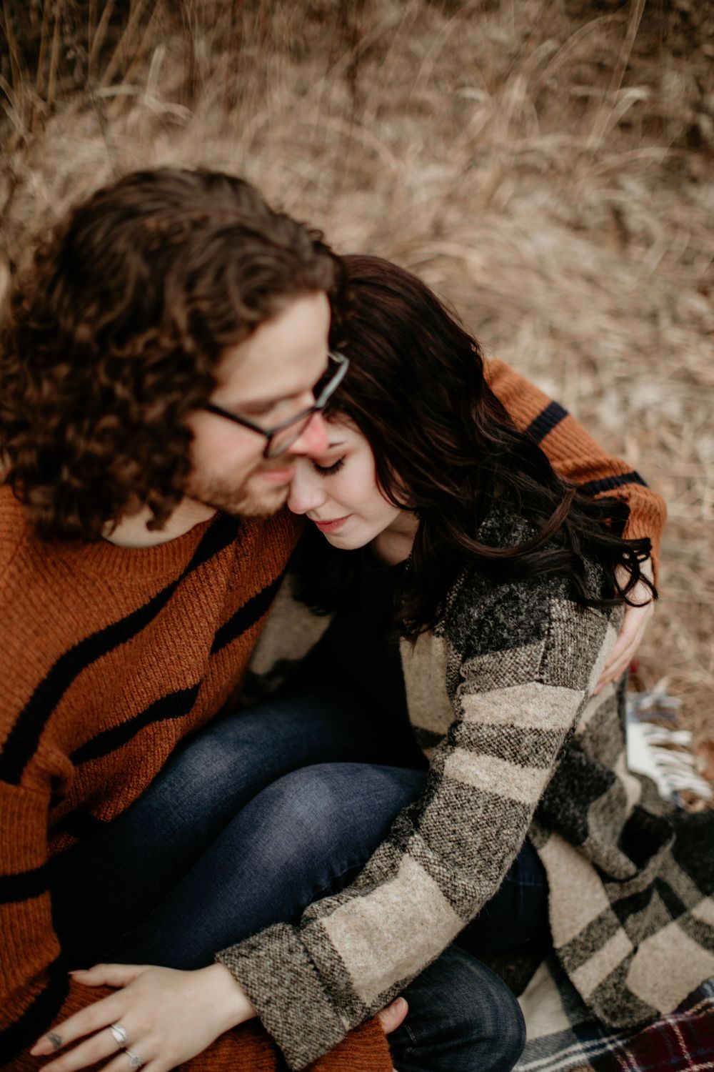 Couple in cozy sweaters sharing an intimate moment, man kissing womans temple in golden grass field.
