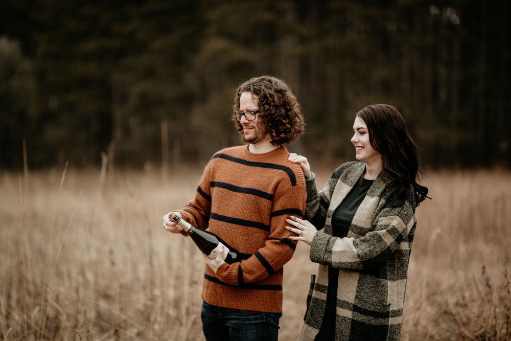 Happy couple smiling and laughing together in an open golden field, woman in plaid jacket holding book.