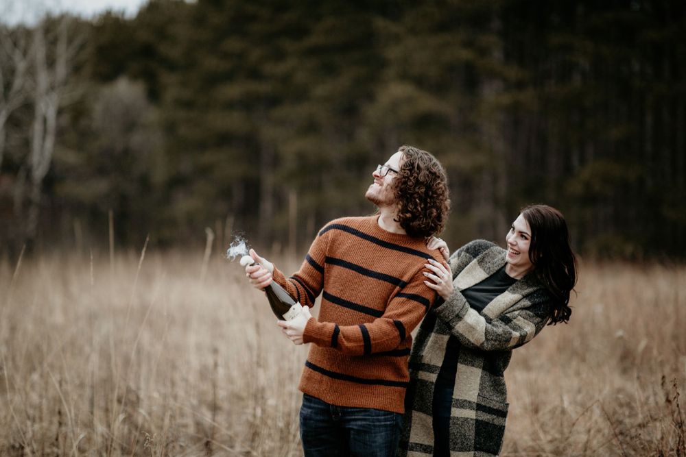 Couple embracing and laughing together in a golden autumn field with trees in the background.