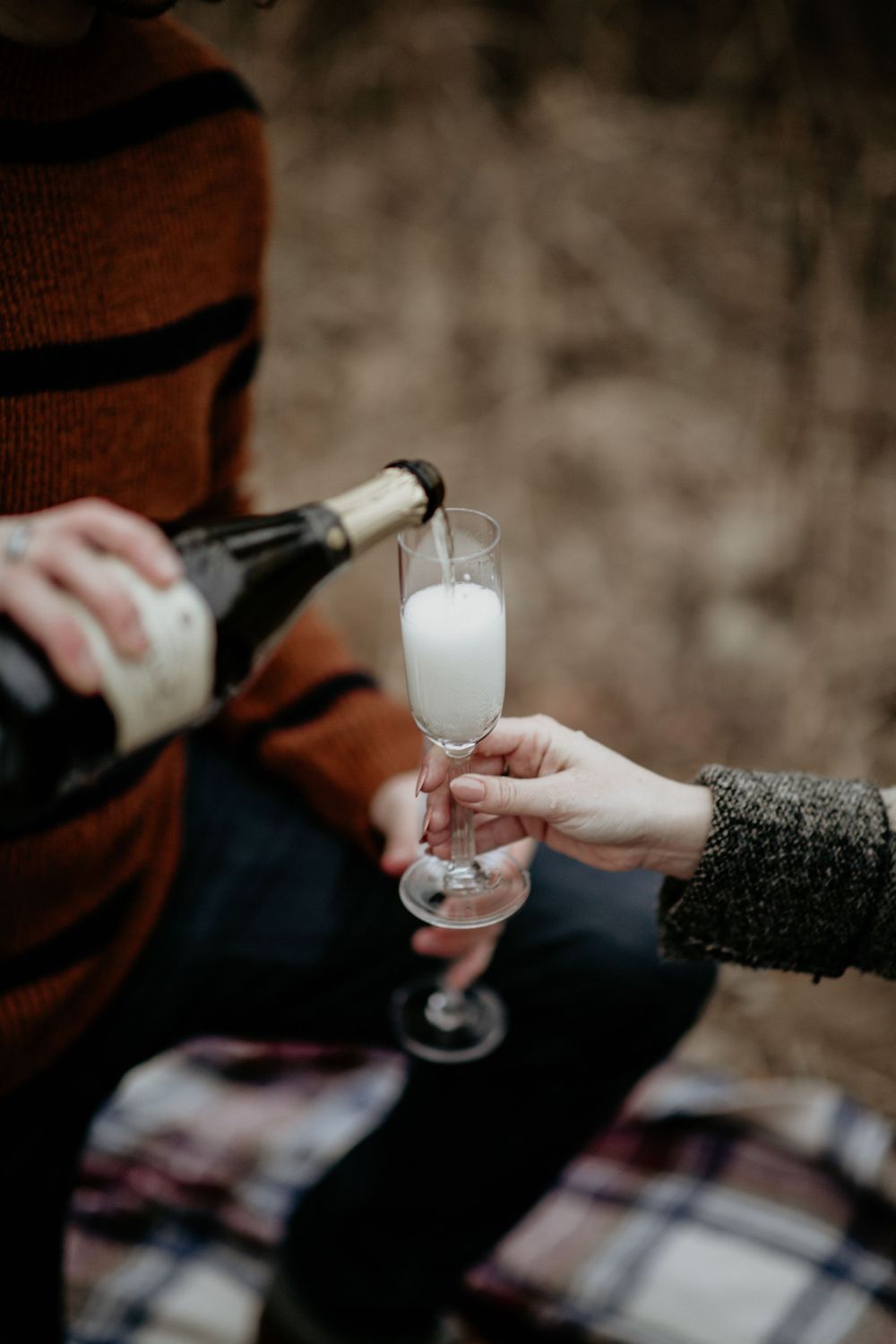 Person pouring champagne into a flute glass outdoors during a romantic fall picnic celebration.