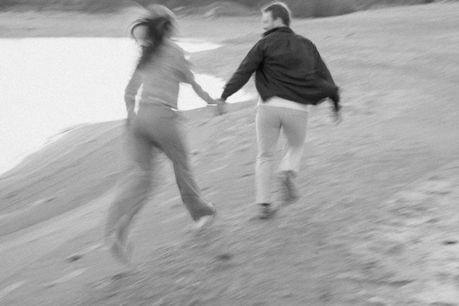 Blurred motion shot of a couple running along the beach holding hands in black and white.