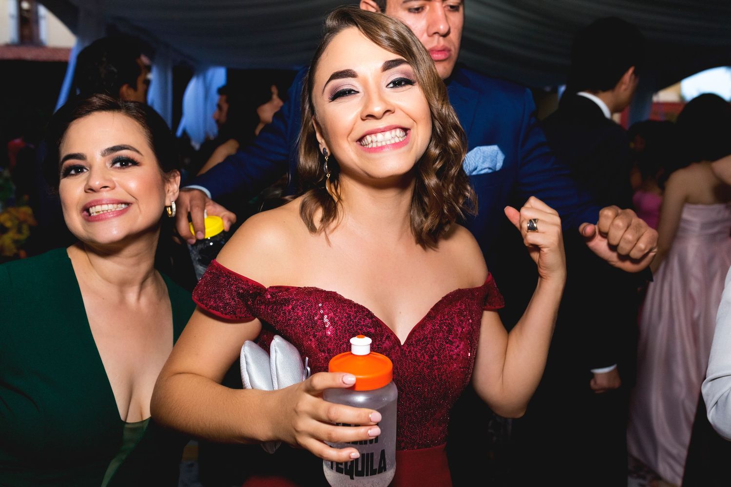 Partygoers in evening attire dancing and celebrating with drinks at a festive event.