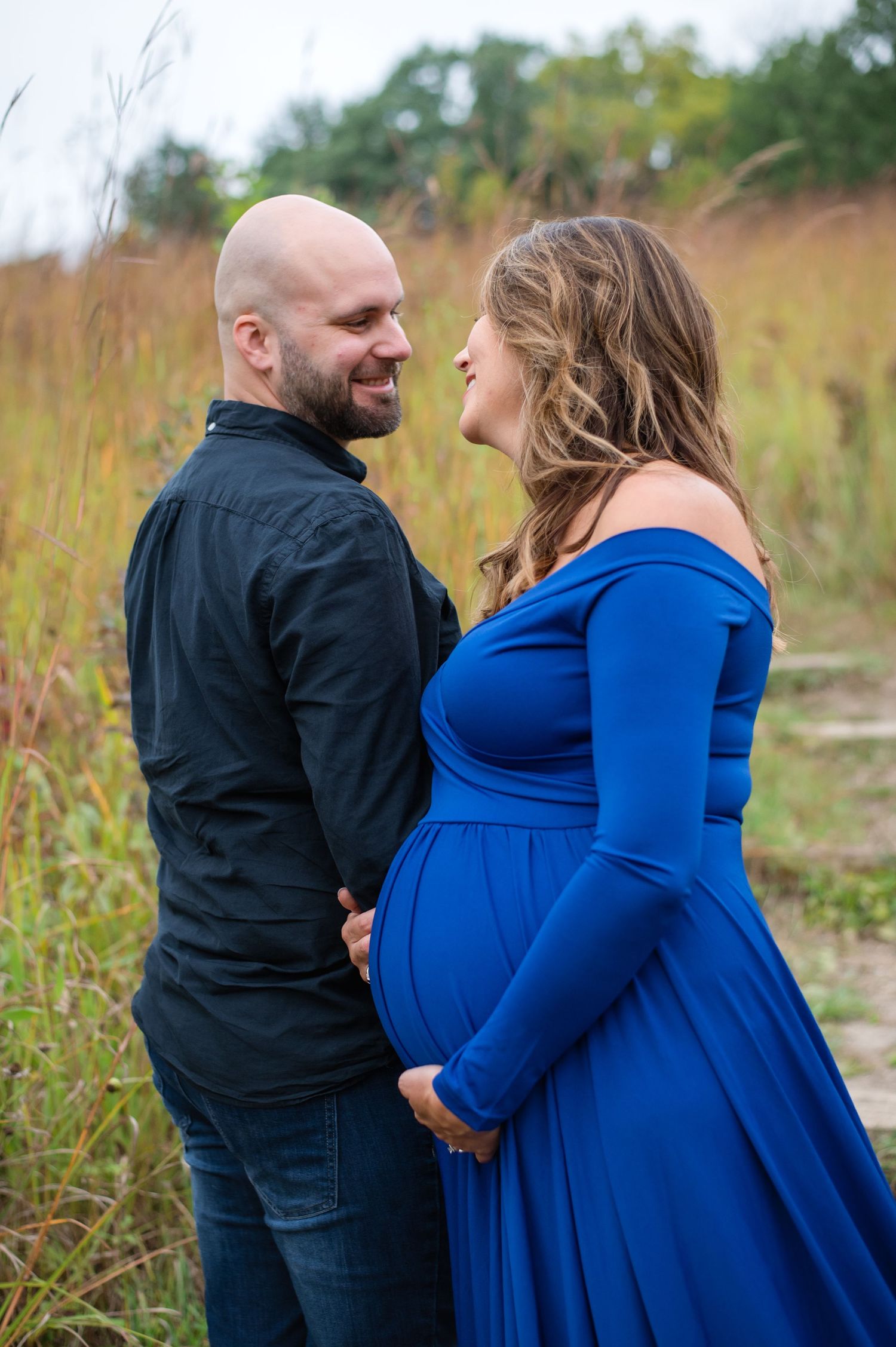 Romantic maternity photo of couple laughing together in golden field at sunset.