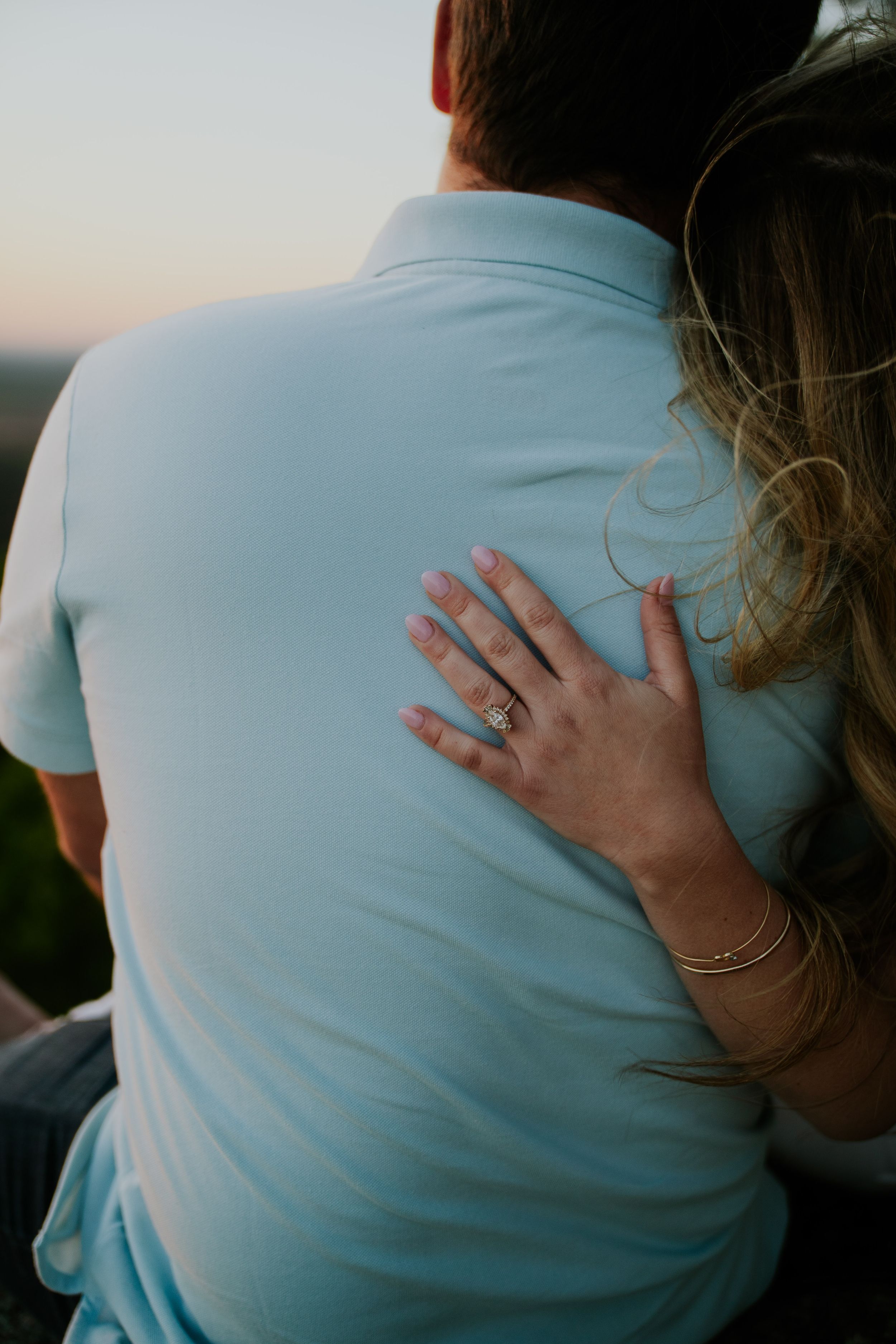 Close-up view of hands resting on a light blue shirt against a sunset backdrop.
