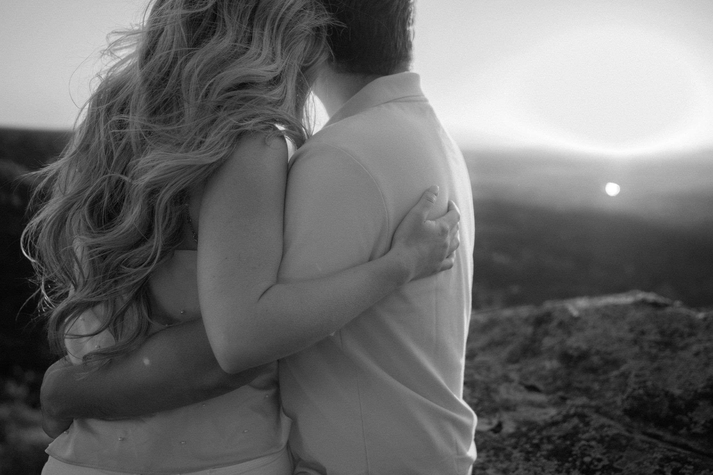 Black and white silhouette of embracing couple with sunset in background.