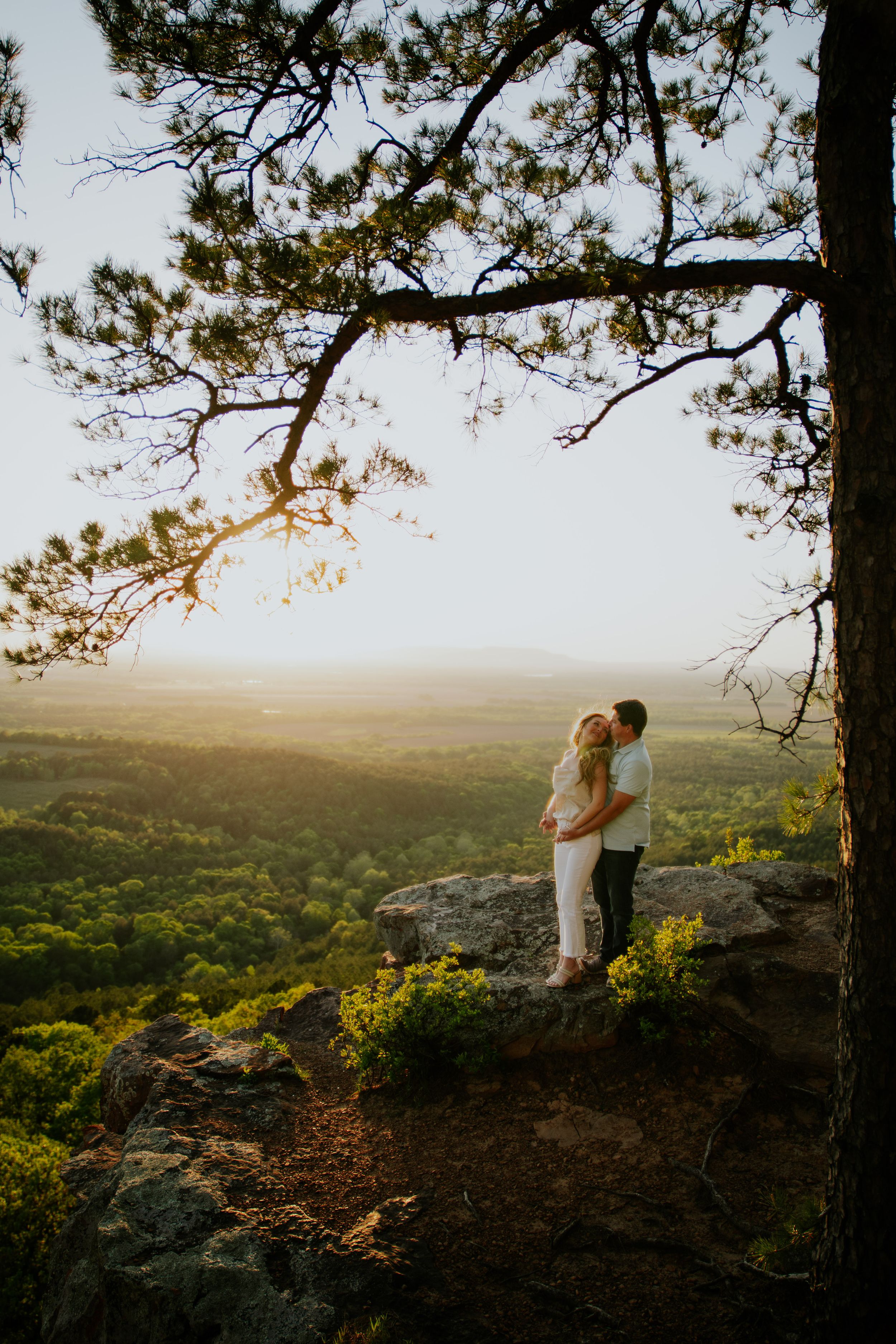 Couple sharing an intimate moment on a scenic overlook surrounded by pine trees.