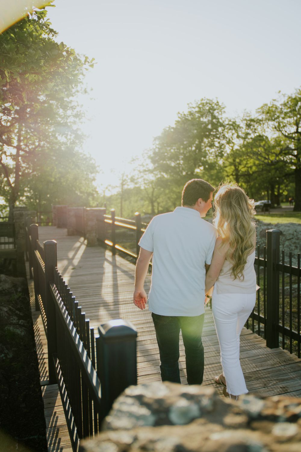 Couple walking along a sunlit pathway with iron railings during golden hour.