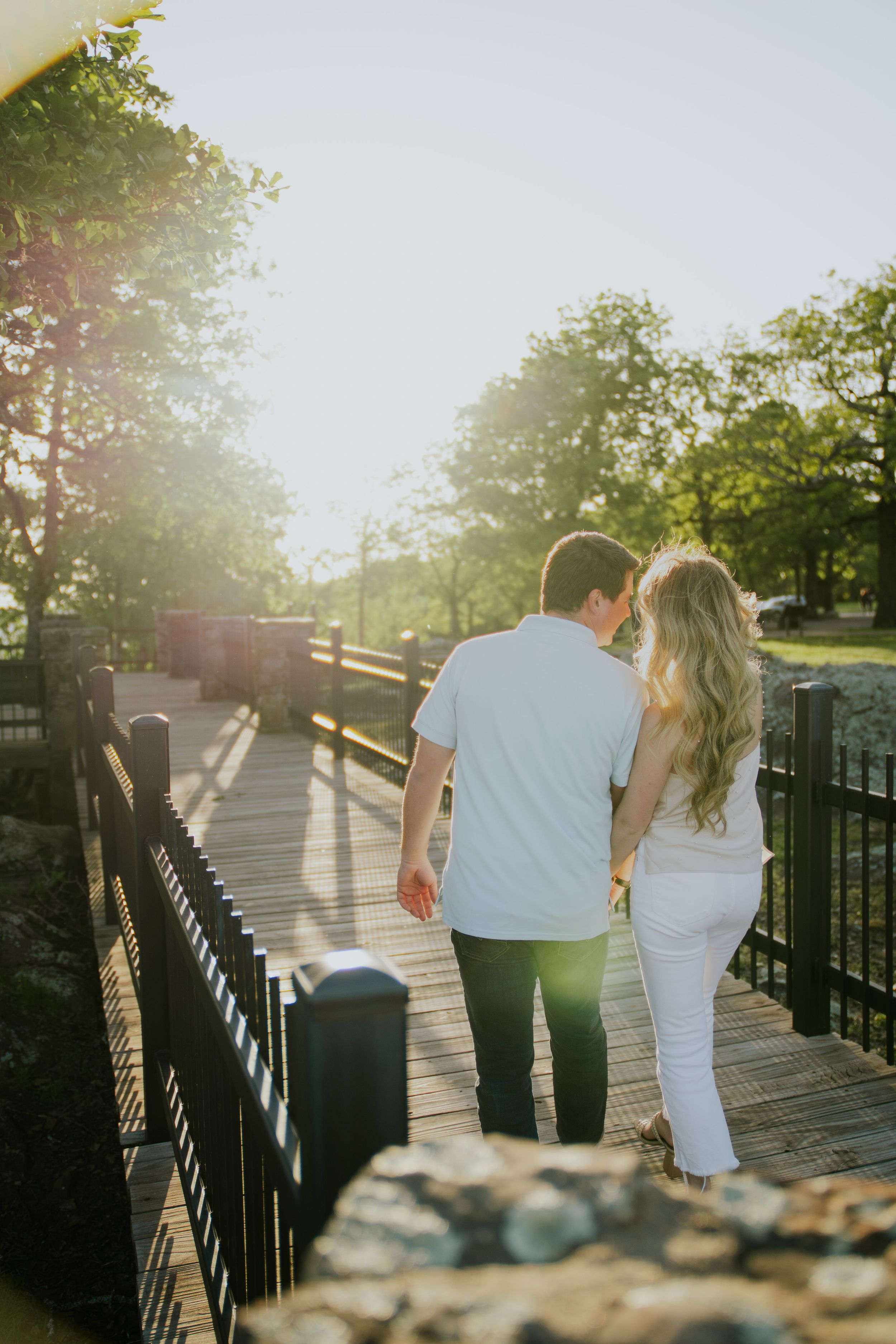 Couple walking along a sunlit pathway with iron railings during golden hour.