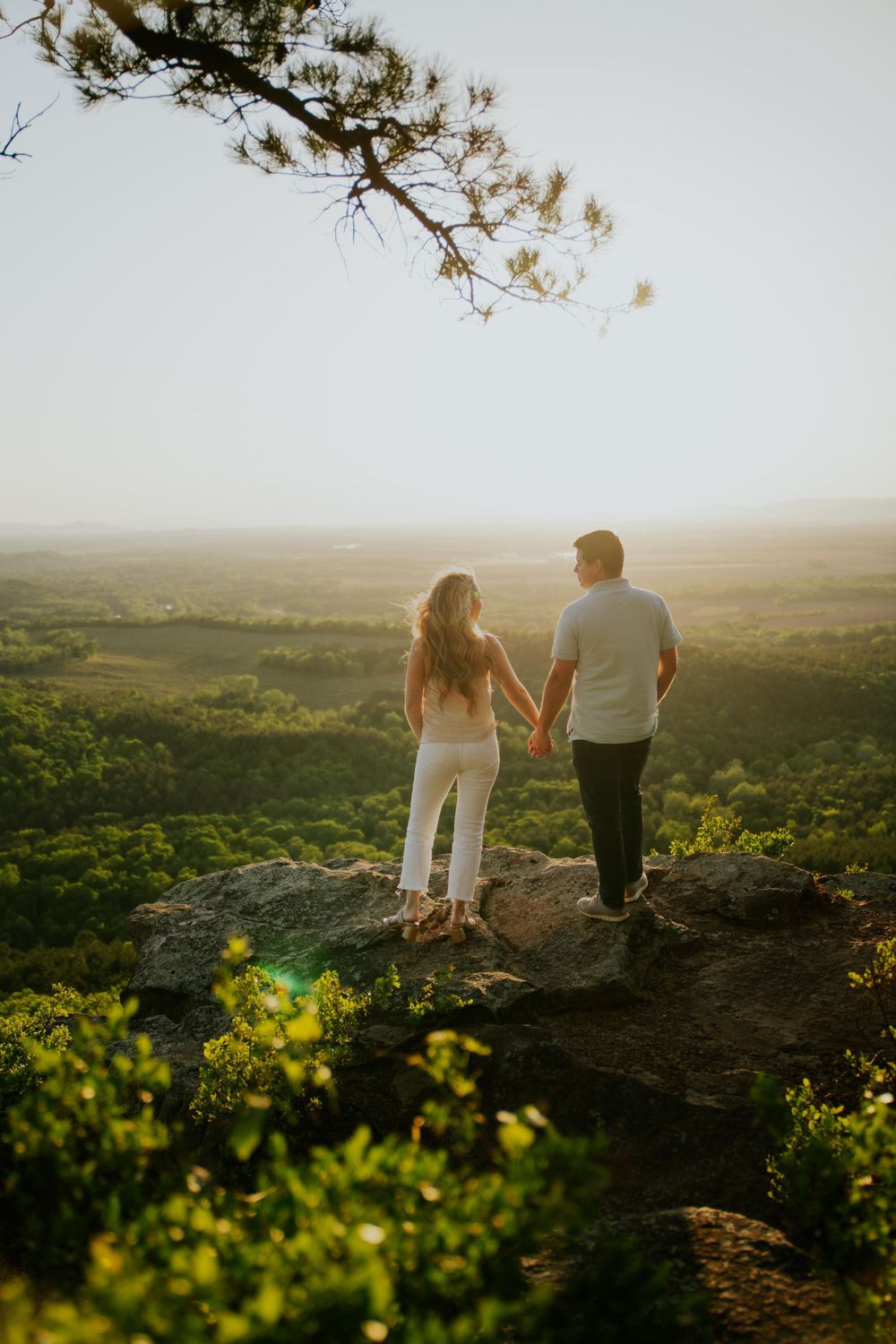 Couple holding hands while overlooking scenic valley at sunset.