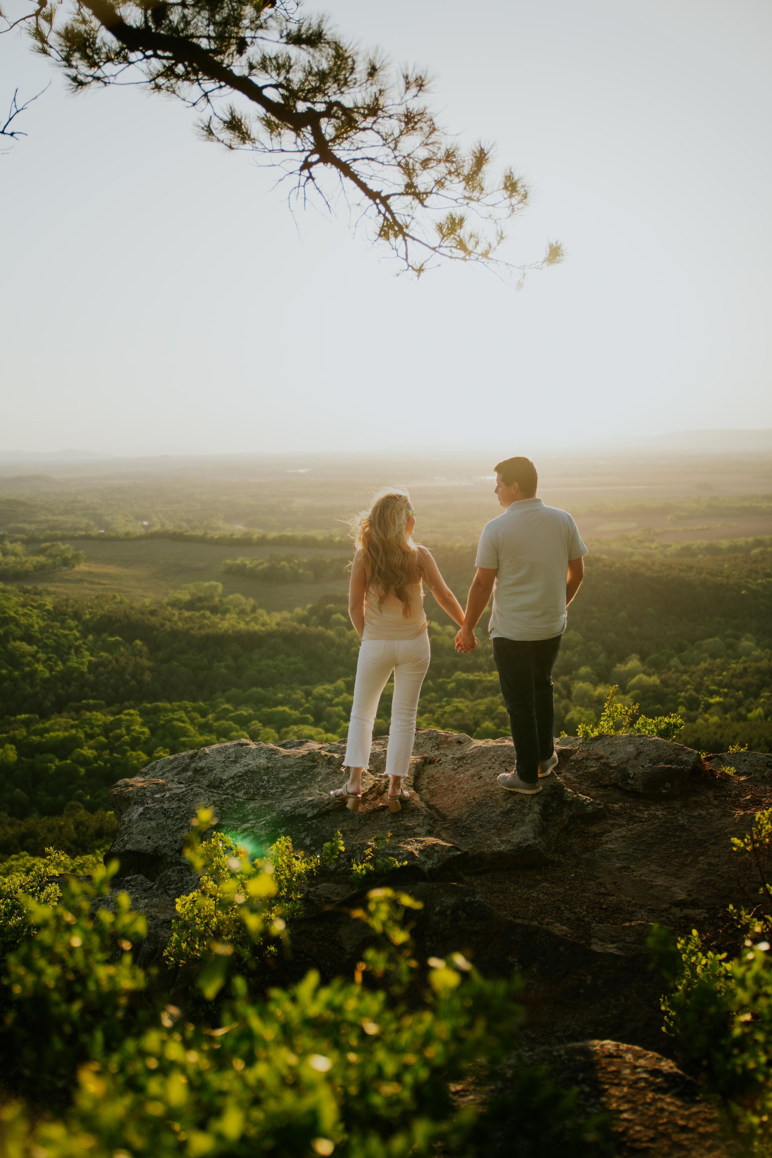 Couple holding hands while overlooking scenic valley at sunset.