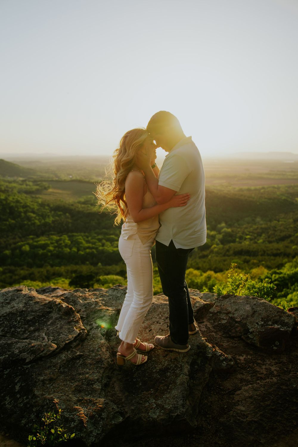 Couple embracing on a scenic mountaintop overlook during sunset.
