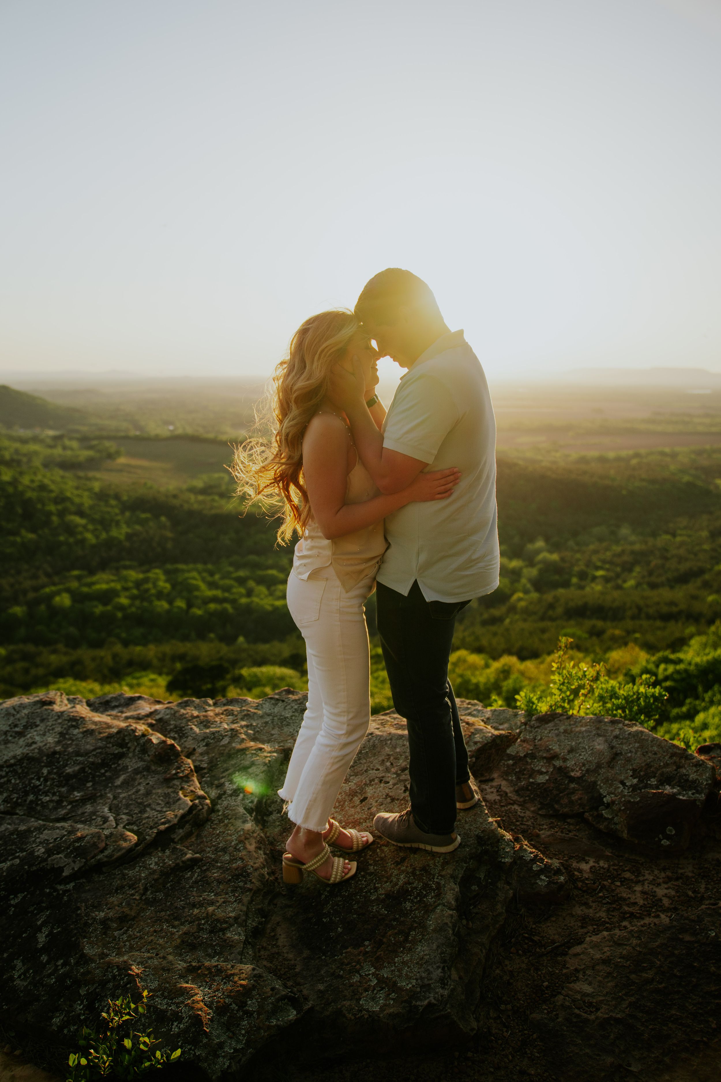 Couple embracing on a scenic mountaintop overlook during sunset.