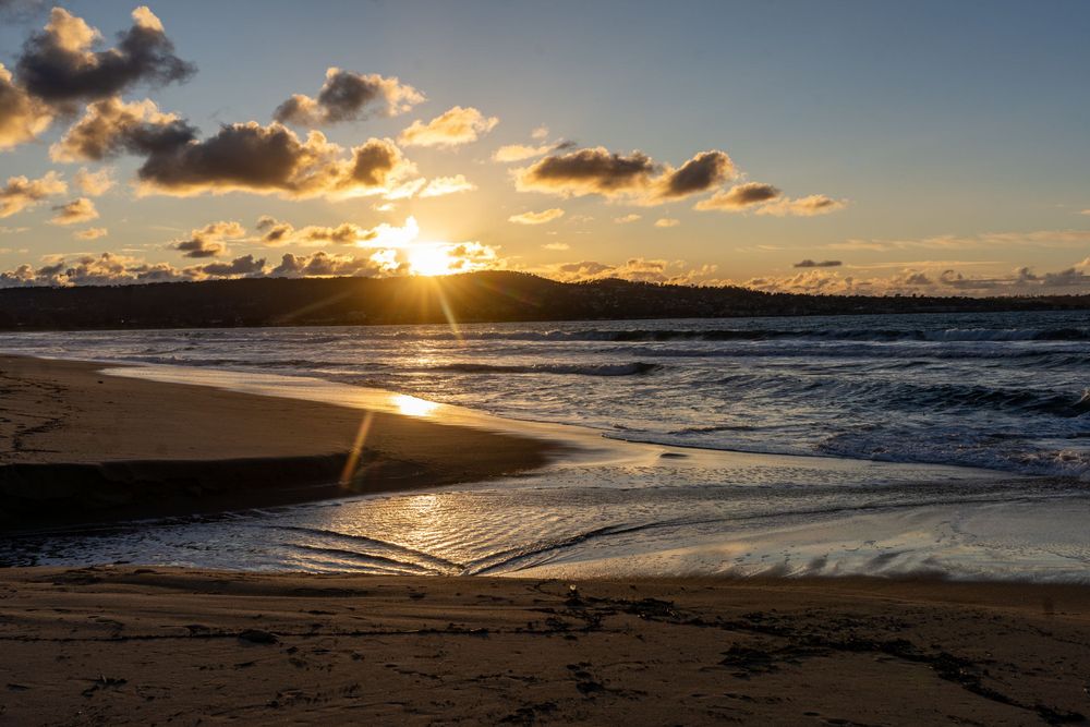 Dramatic sunset over a beach with waves rolling in and clouds silhouetted against the orange sky.