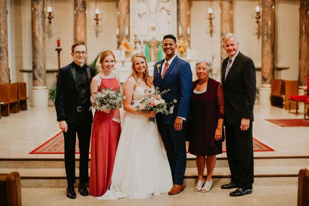 Bride and groom pose with four family members inside decorated church after wedding.