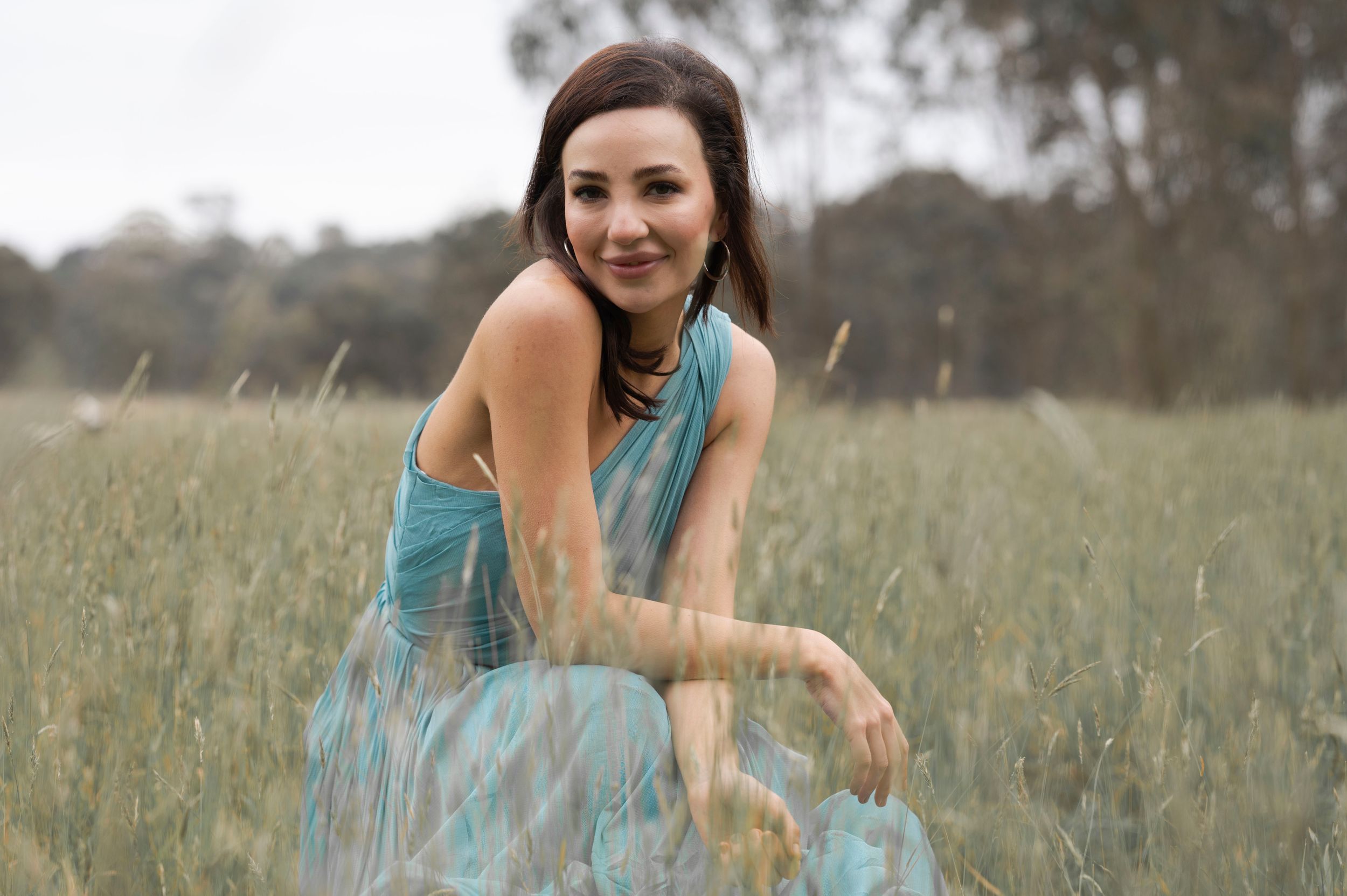 Happy woman in flowing teal dress posing gracefully in a wide open grassy field.