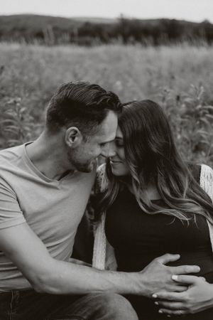 An intimate black and white portrait of an expectant couple sharing a tender moment outdoors.