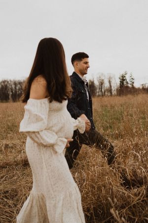 A couple in contrasting outfits walks through autumn fields during a photo session.