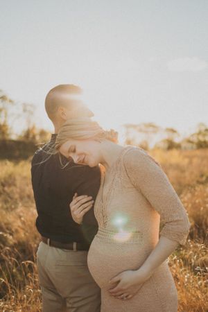 Romantic maternity photoshoot of couple embracing in a sun-lit field during golden hour.