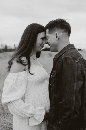 A romantic couple shares an intimate moment in a field wearing contrasting white dress and denim jacket.