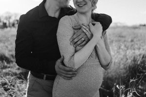 Intimate black and white maternity photo of couple sharing a tender moment outdoors.