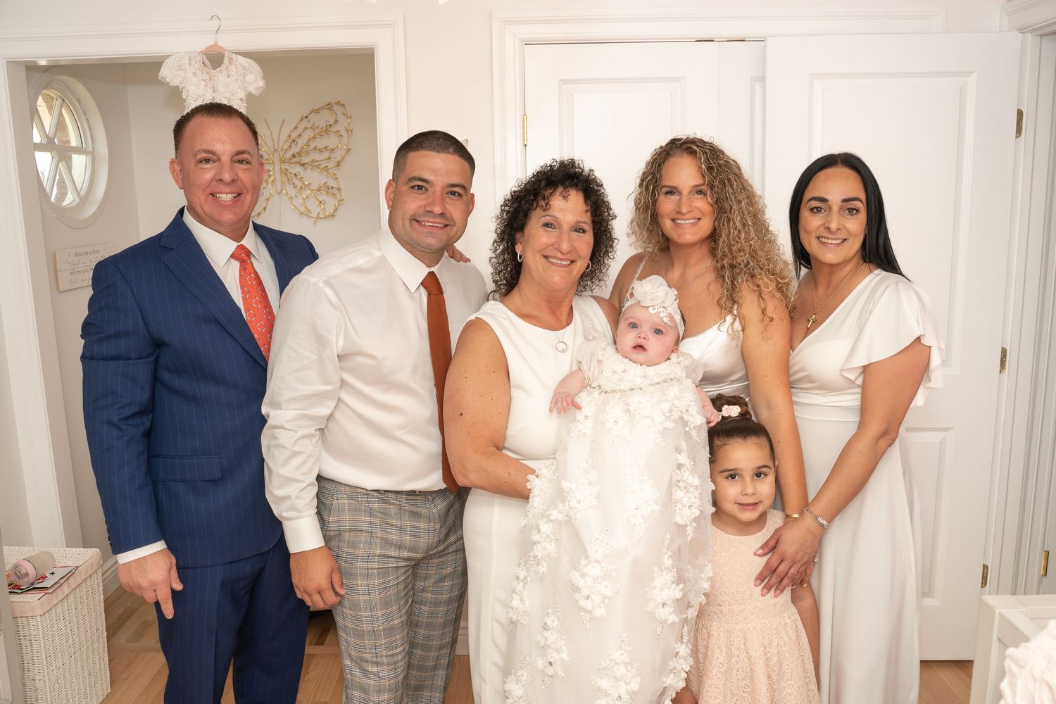 Extended family gathering in formal white and gray attire for a special occasion.