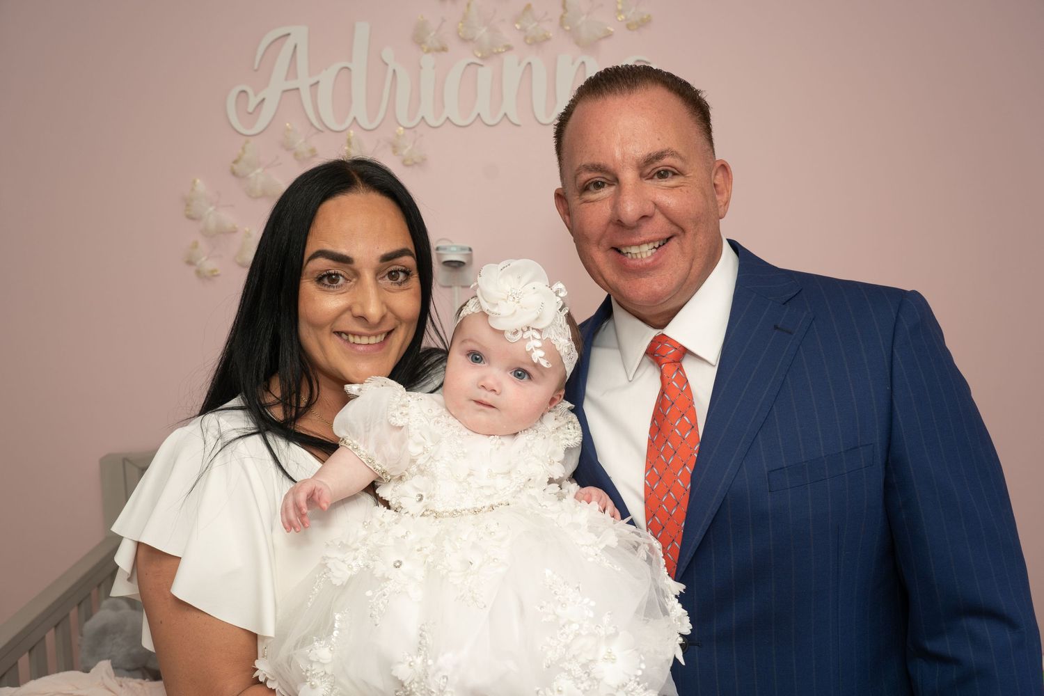Group portrait of people in white and formal attire against a pink backdrop.