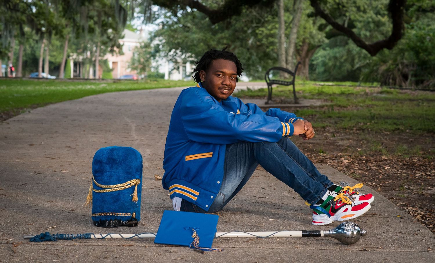 Student sitting on park path with backpack and sneakers in casual blue outfit near trees.