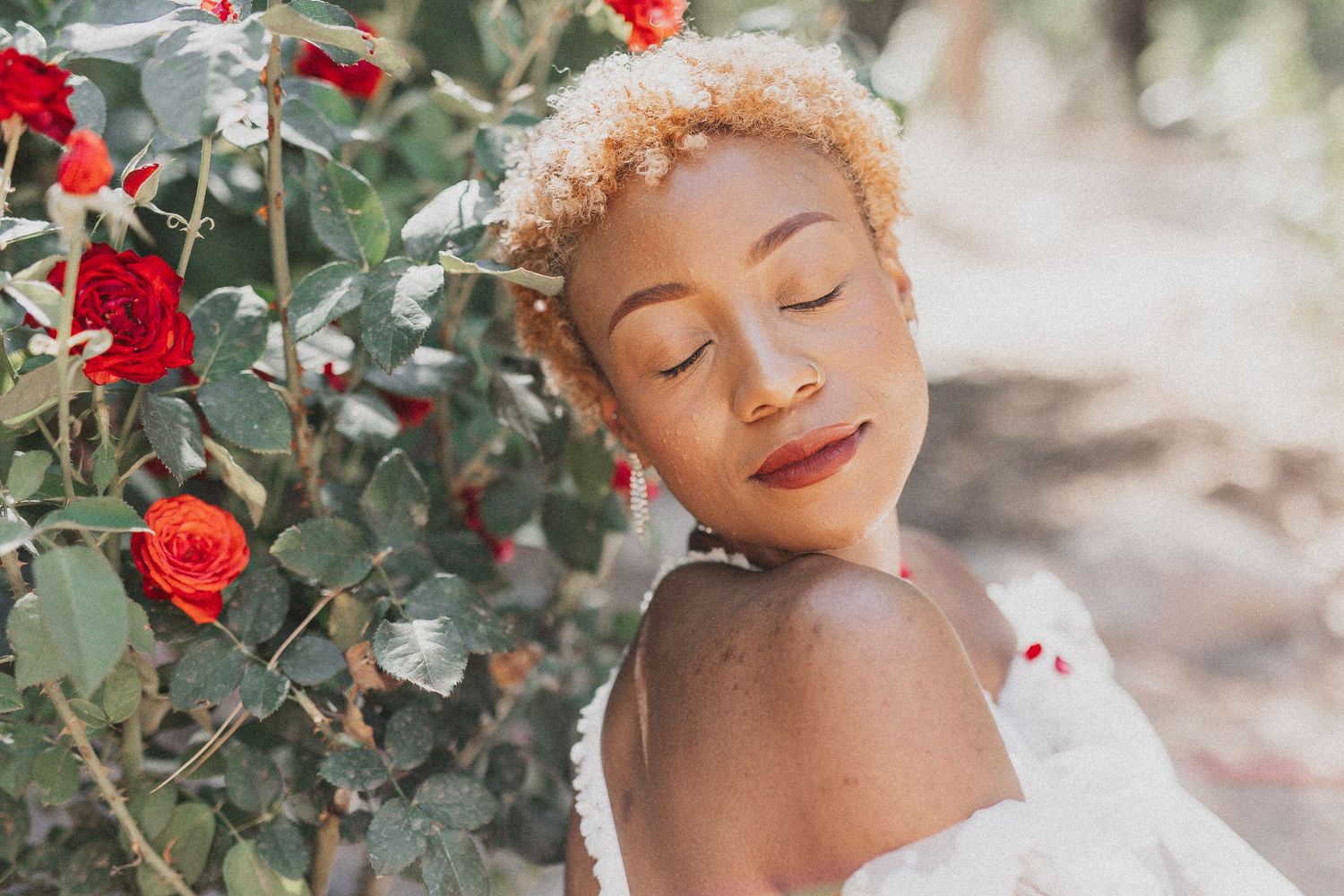 Serene portrait of woman with short blonde hair next to blooming red roses.