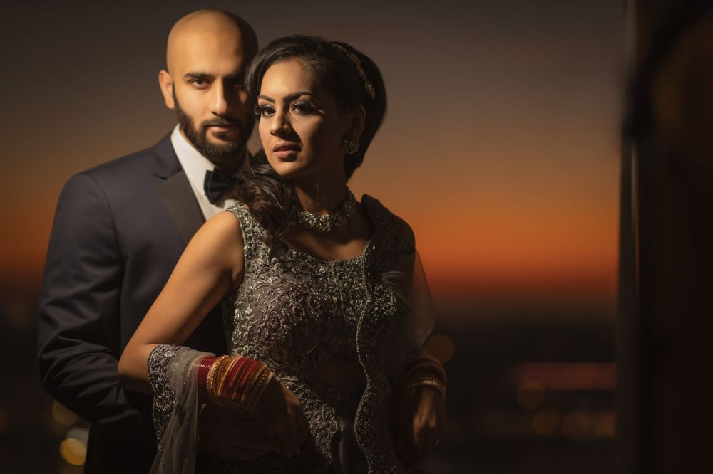 Dramatic sunset portrait of couple in formal evening wear against orange sky.
