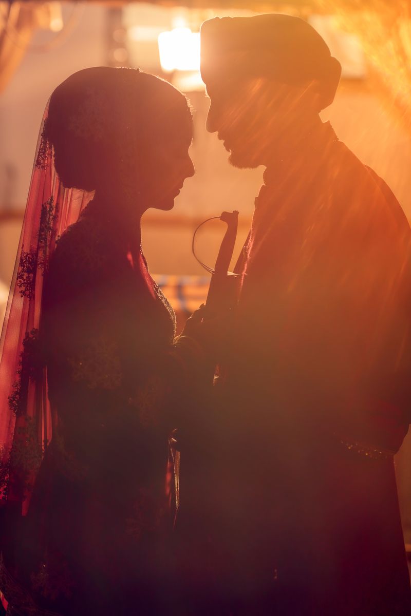 Romantic silhouette of couple in traditional wedding attire against warm sunset lighting.