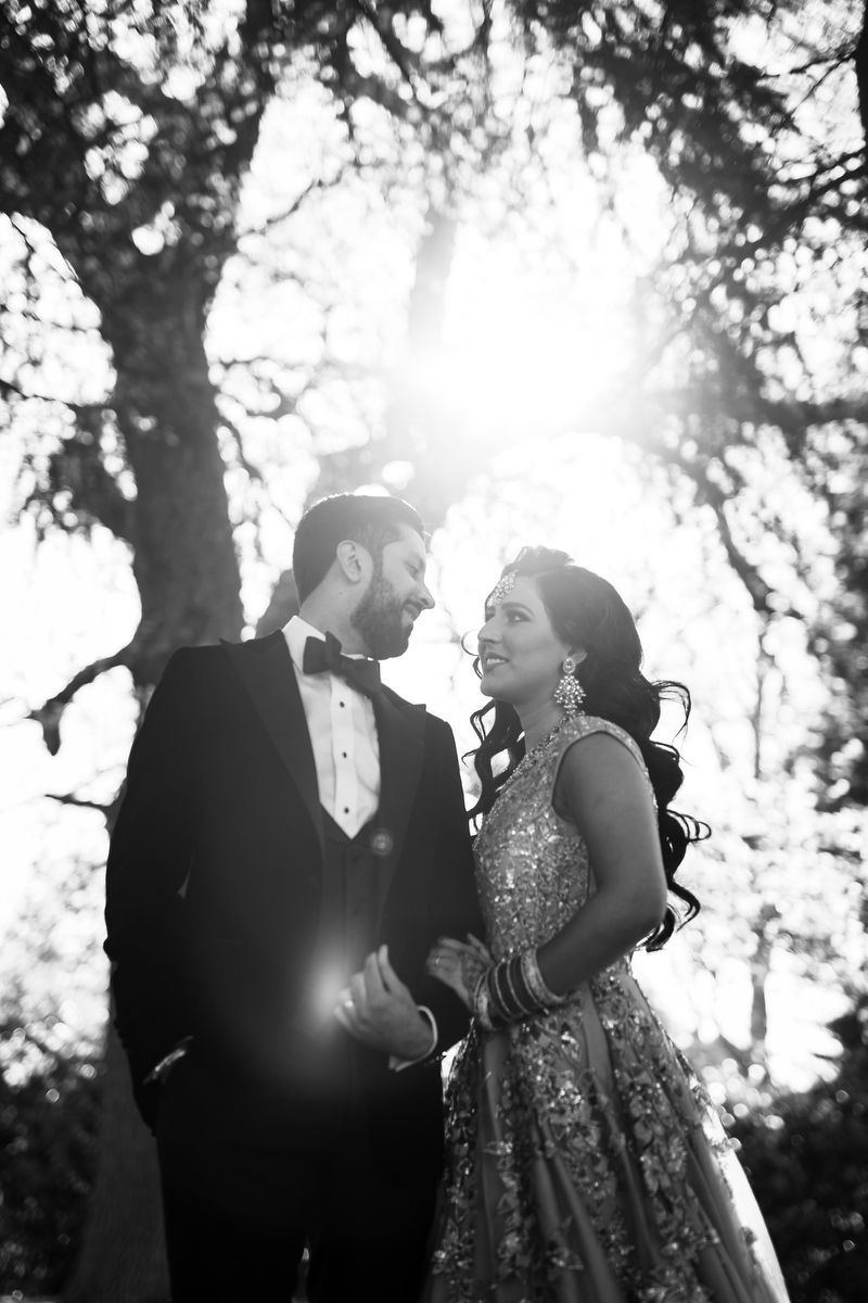 Backlit black and white portrait of couple laughing together under a majestic tree.
