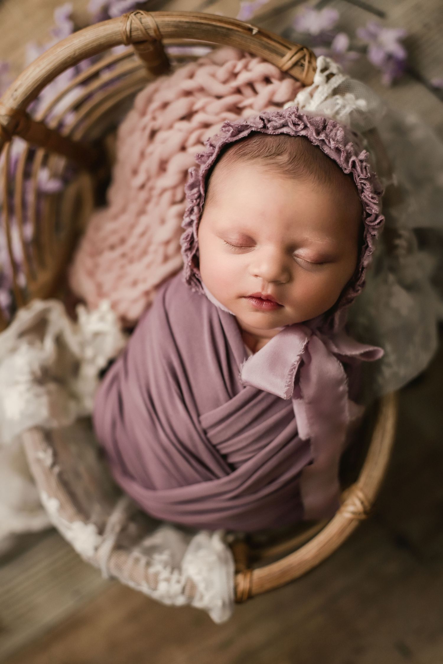 Newborn baby girl portrait in bamboo prop with purple and lace layers