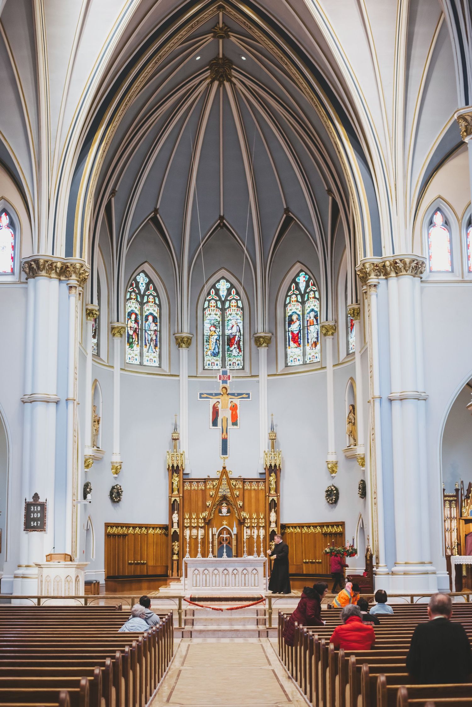 Interior of a gothic cathedral with vaulted ceilings, stained glass windows, and wooden pews leading to the altar.