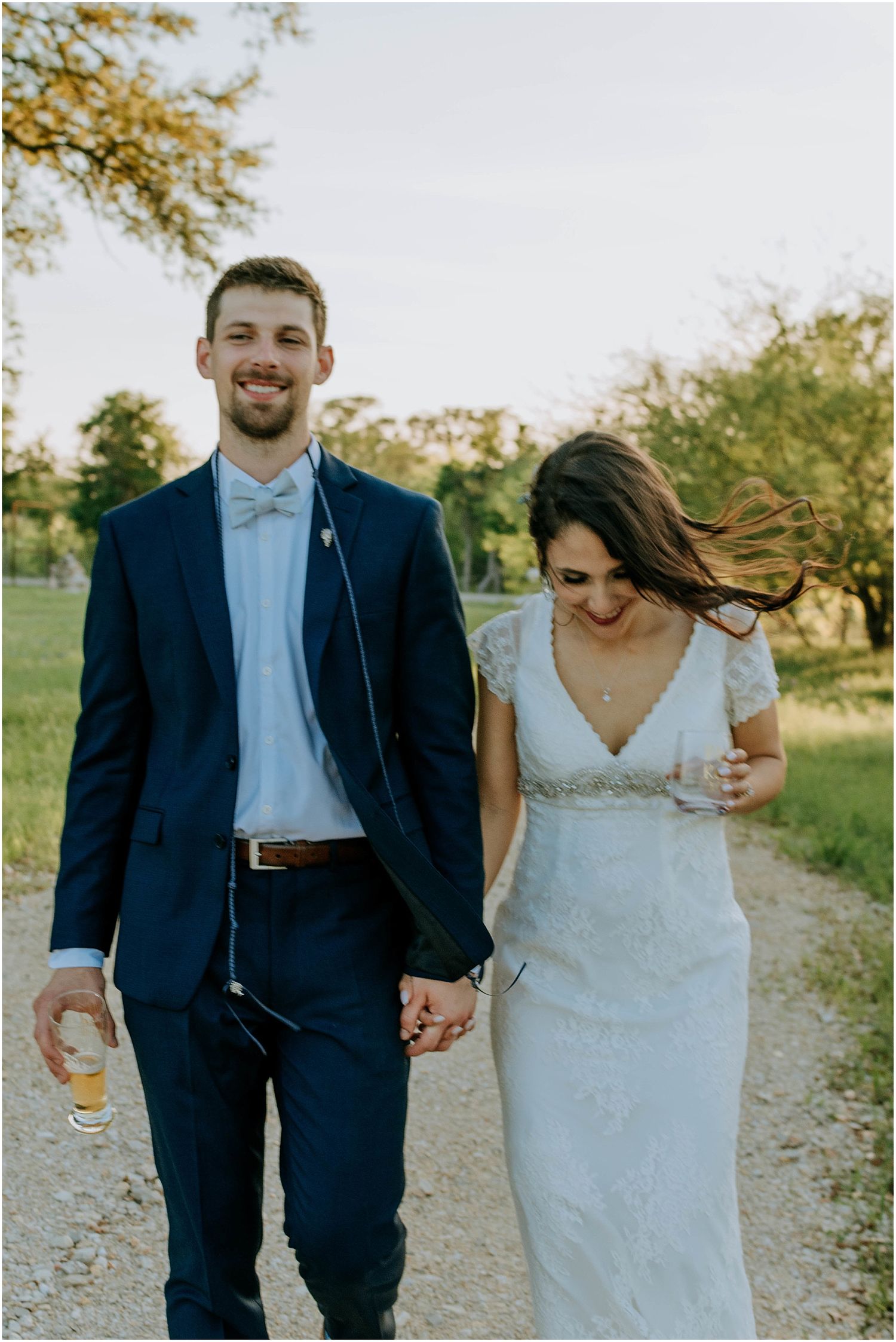 Candid moment of newlyweds walking together on a sunny path with bride in lace gown.