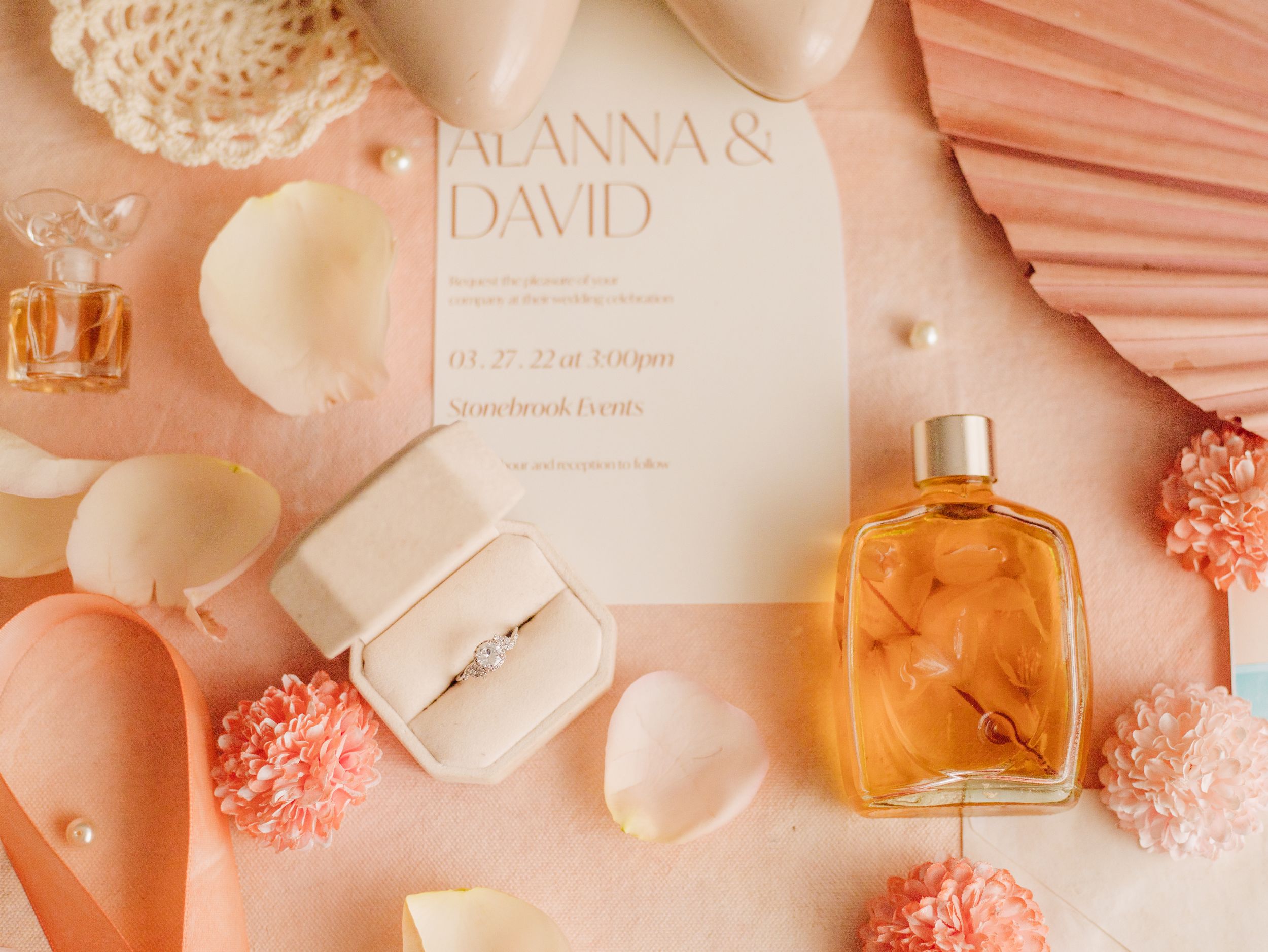 Flat lay of wedding stationery and perfume bottles in soft peach and coral tones.